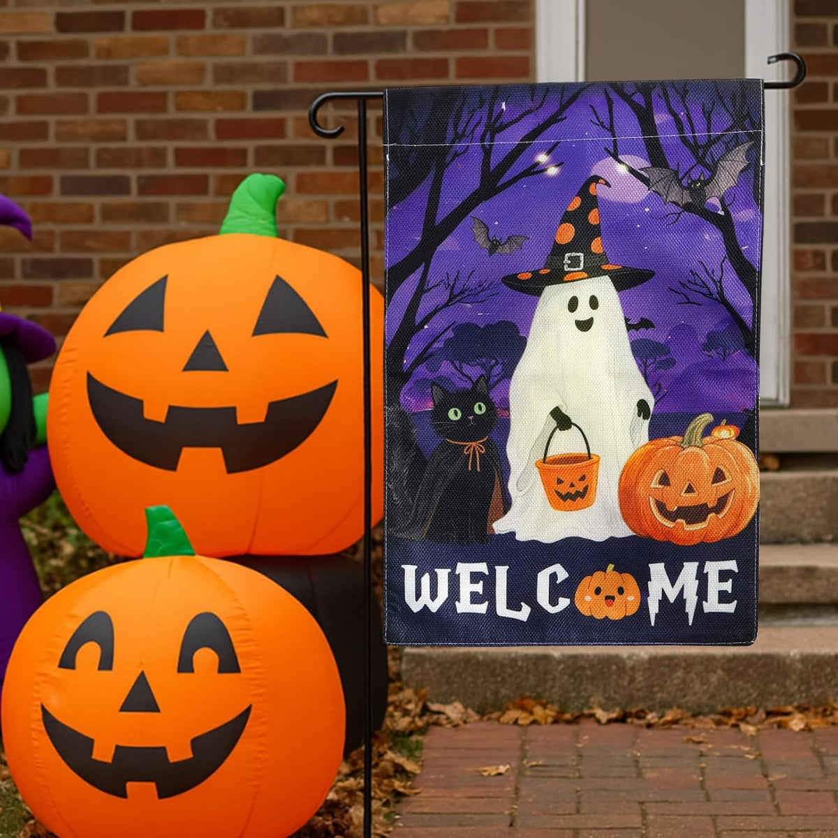 Ghost welcome garden flag next to inflatable jack-o'-lanterns